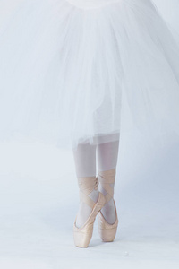 一个女孩站在伸出的腿上，穿着尖鞋。 一个穿着白色裙子跳舞和白色紧身衣的孩子。 脚在尖角。 芭蕾舞学校的练习。 芭蕾课。 白色背景
