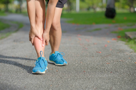 年轻的健身妇女抱着他的运动腿受伤肌肉在训练中疼痛。 亚洲跑者在夏季外出跑步和运动后小腿疼痛和有问题