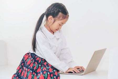 小快乐的孩子用笔记本电脑坐在白色沙发上。 童年生活方式。