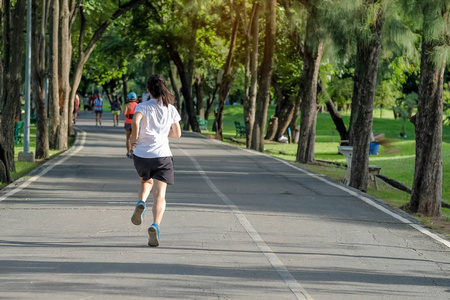 年轻的健身妇女在公园跑步，户外女跑步者在亚洲运动员外面的路上散步，在阳光明媚的早晨在小径上慢跑和锻炼。 运动健康及健康概念