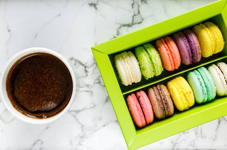 一杯咖啡和绿色盒子，上面有五颜六色的马卡龙和大理石桌子背景上的咖啡杯。 美味的糖果和咖啡休息