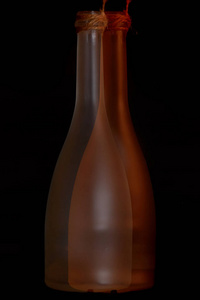 两瓶酒哑光与橙色棕色闪烁接近。 瓶子相交。 黑色背景