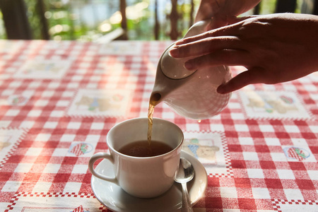 女孩把茶倒在杯子里。桌上的一杯茶。一杯新鲜煮的红茶, 逃逸蒸汽, 温暖柔和的光线