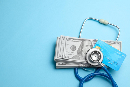 蓝色背景上的现金美元和带有听诊器的信用卡。医疗链球或昂贵的药品的概念, 医生的工资
