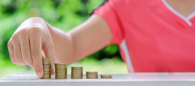 女人的手在早晨的阳光下把硬币金币叠在木桌上。 商业投资退休金融和为未来概念储蓄资金