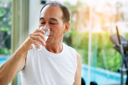 老年人运动后在健身房健身中心喝矿泉水。 老年人健康的生活方式。