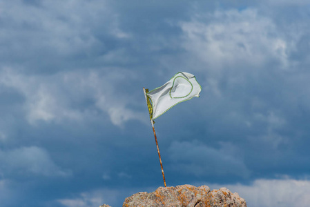 山顶上的白色旗帜。 蓝天和云彩。 旗帜在风中飘扬。 山顶的岩石。 云彩