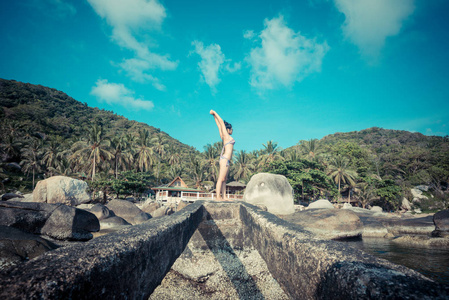 运动型亚洲女性在岩石海海岸线上做瑜伽运动夏季景观