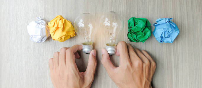 手拿双灯泡或灯与彩色皱纸在木桌上。新理念创意天才和创新理念