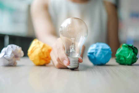 商务女性手拿灯泡或灯与彩色皱纸在木桌上。新理念创意天才和创新理念