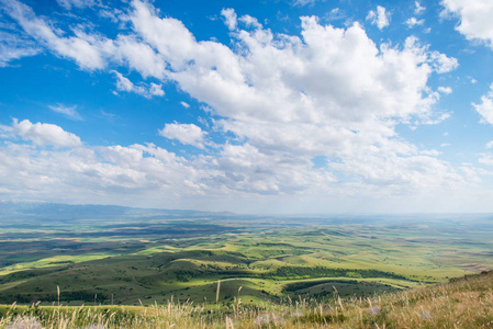 小山地平线蓝天白云.白色卷云被太阳照亮.高原上绿油油的小山丘.