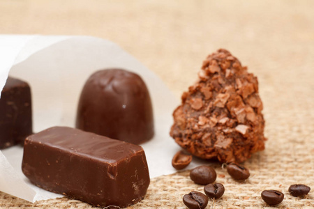 巧克力糖果，各种形状的咖啡豆和白纸包在桌子上用麻布。 浅场深。