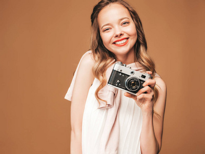 开朗的年轻女人的肖像，带着灵感拍照，穿着白色连衣裙。 拿着复古相机的女孩。 模特摆在金色背景上