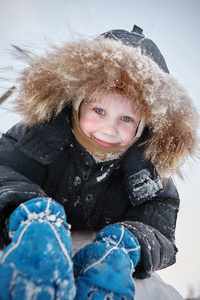 一个穿着温暖衣服的男孩躺在雪地上微笑着看着相机。