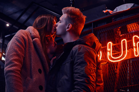着热情的年轻夫妇接吻, 而站在咖啡馆与工业内饰, 背光招牌在背景照片