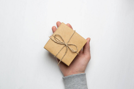 s hand holds a gift in a box on a white wooden background