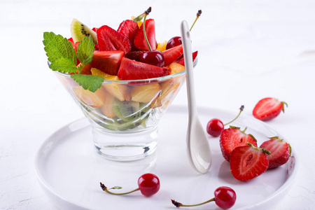 新鲜美味的混合水果沙拉在玻璃碗白色桌子背景。 健康维生素早餐