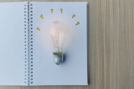 木桌上有笔记本的灯泡或灯。 新观念创新天才和创新观念