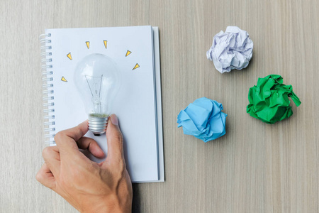 手拿灯泡或灯与彩色皱纸在木桌上。 新观念创新天才和创新观念