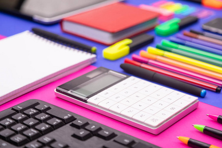 平面平面组成的商务办公桌与键盘, 计算器, 贴纸, 和笔在五颜六色的粉红色和蓝色的背景