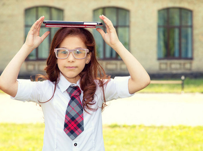 女学生头上拿着一本书和一块数字平板电脑在一所学校建筑学院的后面。