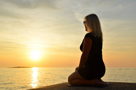 日落时分，坐在海边瑜伽姿势的女人。