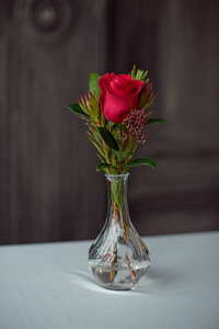花瓶里放着一朵红玫瑰，桌上放着一张白色的桌布