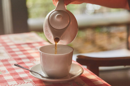 女孩把茶倒在杯子里。桌上的一杯茶。一杯新鲜煮的红茶, 逃逸蒸汽, 温暖柔和的光线