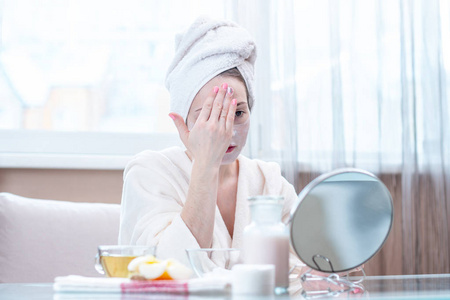 美丽快乐的年轻女人,头上有一条毛巾,在脸上涂上天然化妆品,滋润皮肤