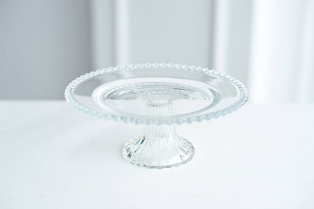 玻璃圆台上装饰着玻璃球，用来做蛋糕和甜点，放在白色背景的白色桌子上。
