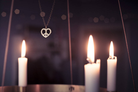 和平，爱，圣诞节背景与一个和平的心符号吊坠挂在蜡烛发光的金色冒险吊灯。粉色过滤器。