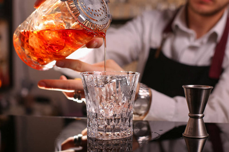 专业调酒师准备橙色鸡尾酒专业的酒保把鸡尾酒从钢制的摇床上倒入一个