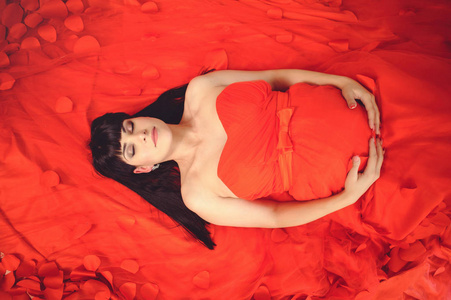 新的生活理念..怀孕，母性和幸福。穿红色背景的时尚优雅红色连衣裙的孕妇特写图像