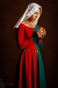 一个美丽的女孩在棕色背景上穿着红色和绿色的中世纪礼服的肖像。爱好中世纪的重建。
