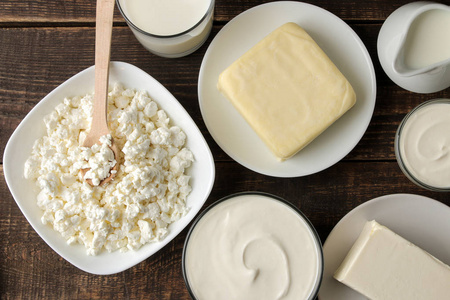 奶制品。牛奶，酸奶油，奶酪，黄油和干酪放在棕色的木桌上。顶部视图