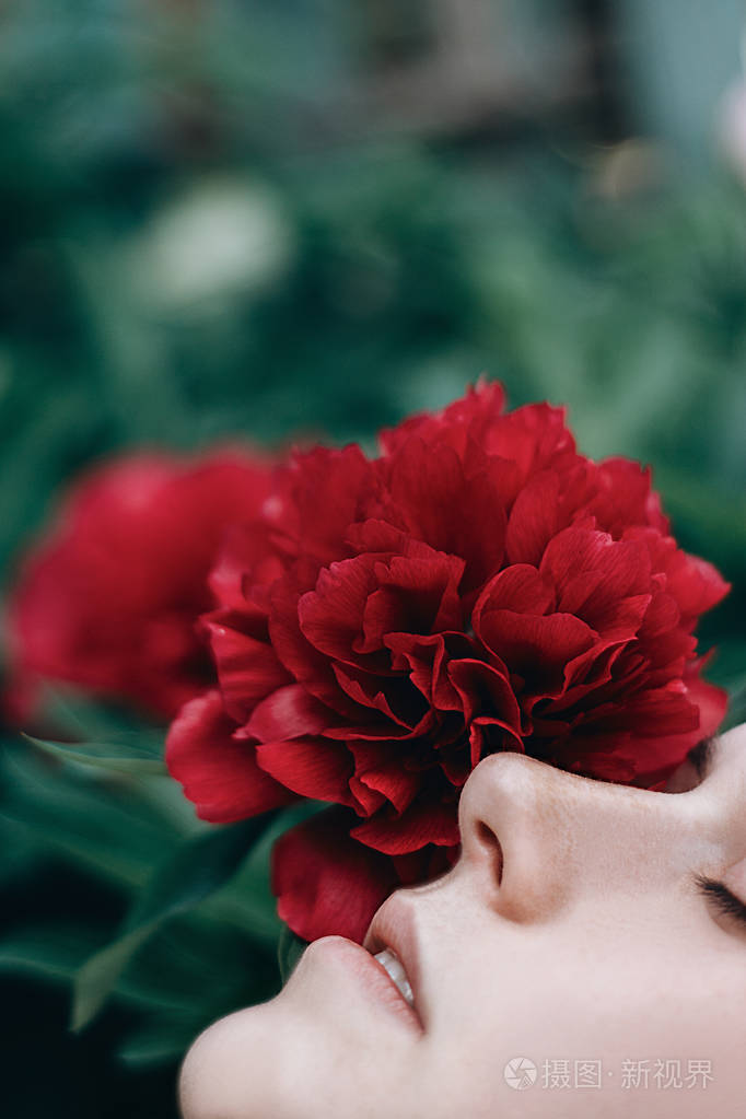美丽而温柔的女孩肖像闭着眼睛在红花牡丹中春天