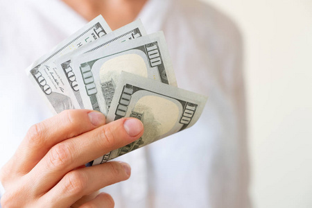 s hand is holding two hundreds of dollars, neutral background