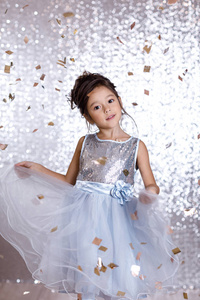 微笑的小女孩在银色礼服上五彩纸屑背景