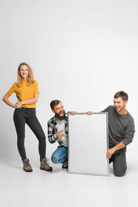 三个逗笑的年轻人穿着休闲时髦的衣服，摆姿势，拿着模型，大白板，孤立在演播室白色背景中
