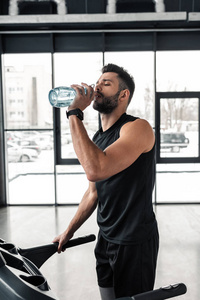 运动中的年轻人在健身房跑步机上喝水