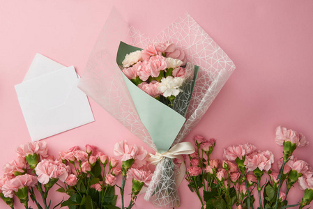 顶部观看美丽的花束，温柔的粉红色花朵和白色信封与卡片隔离在粉红色。