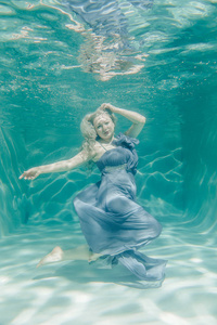 胖乎乎的女人，穿着灰色晚礼服，在假期里在水下游泳，尽情放松