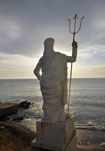 海王星的雕像，上面覆盖着剥落的白色油漆，贴在蓝色的大海和日落的天空背景上