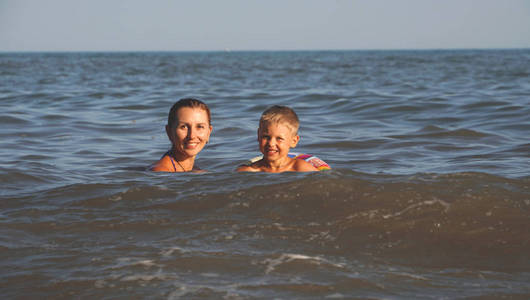 母子在海里游泳。 暑假在海边。 幸福的家庭在海里游泳。 妈妈和孩子在水里。