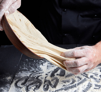 s hands knead white wheat flour dough on black wooden background