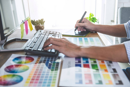 男性创意平面设计师在工作场所使用工作工具和附件进行颜色选择和绘制图形平板的图像。