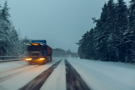 在暮色中, 当雪飞来的时候, 卡车在冬天的路上开着大灯行驶。在危险的条件下驾驶的概念, 冬季能见度差。图片与莫蒂