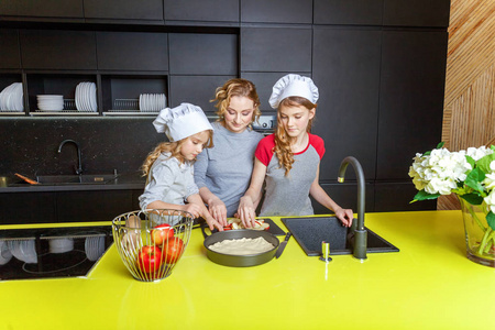 厨房里的幸福家庭。 妈妈和两个孩子准备面团烤苹果派。 妈妈和女儿在家做健康的食物，玩得开心。 家庭团队合作帮助产妇概念
