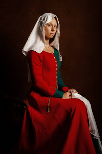 一个美丽的女孩的肖像，穿着一件中世纪的衣服，红色和绿色，棕色背景。 爱好中世纪的重建。