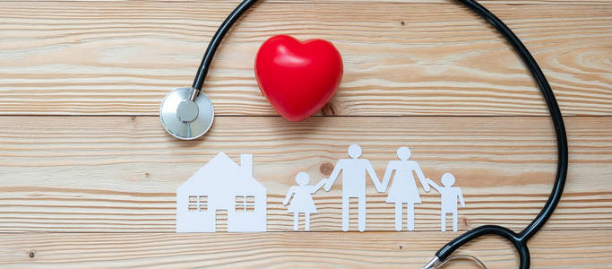 听诊器有红色心形家庭和木制背景上的家纸。 医疗及保险概念